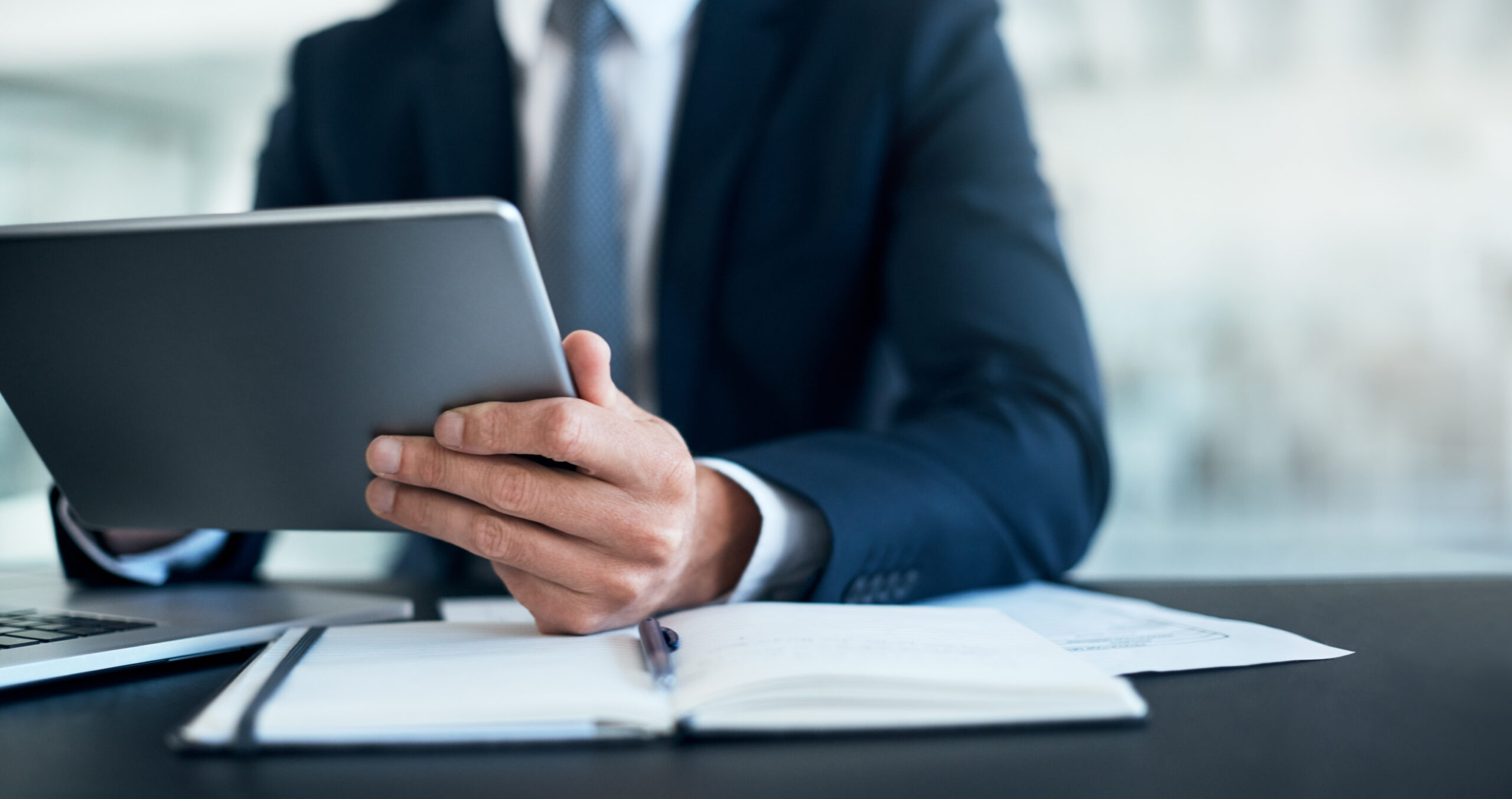 Ausschnitt eines Geschäftsmannes, der ein digitales Tablet an seinem Schreibtisch in einem modernen Büro benutzt